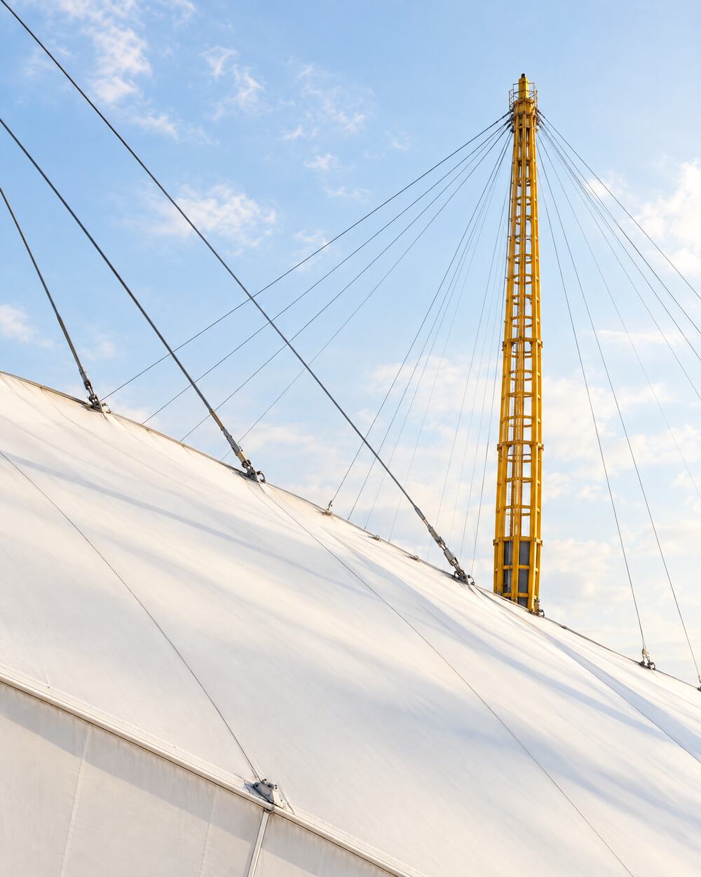 The white canopy and a yellow mast of The O2 against a clear blue sky
